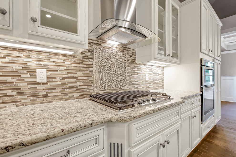 Example of a mid-sized transitional l-shaped dark wood floor open concept kitchen design with a farmhouse sink, recessed-panel cabinets, white cabinets, granite countertops, beige backsplash, mosaic tile backsplash, stainless steel appliances and an island