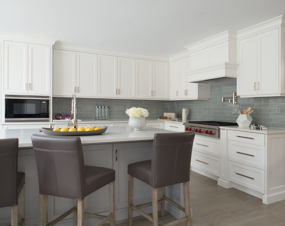 Large transitional l-shaped open plan kitchen in New York with an undermount sink, shaker cabinets, white cabinets, quartz benchtops, grey splashback, ceramic splashback, stainless steel appliances, porcelain floors, with island, beige floor and beige benchtop.