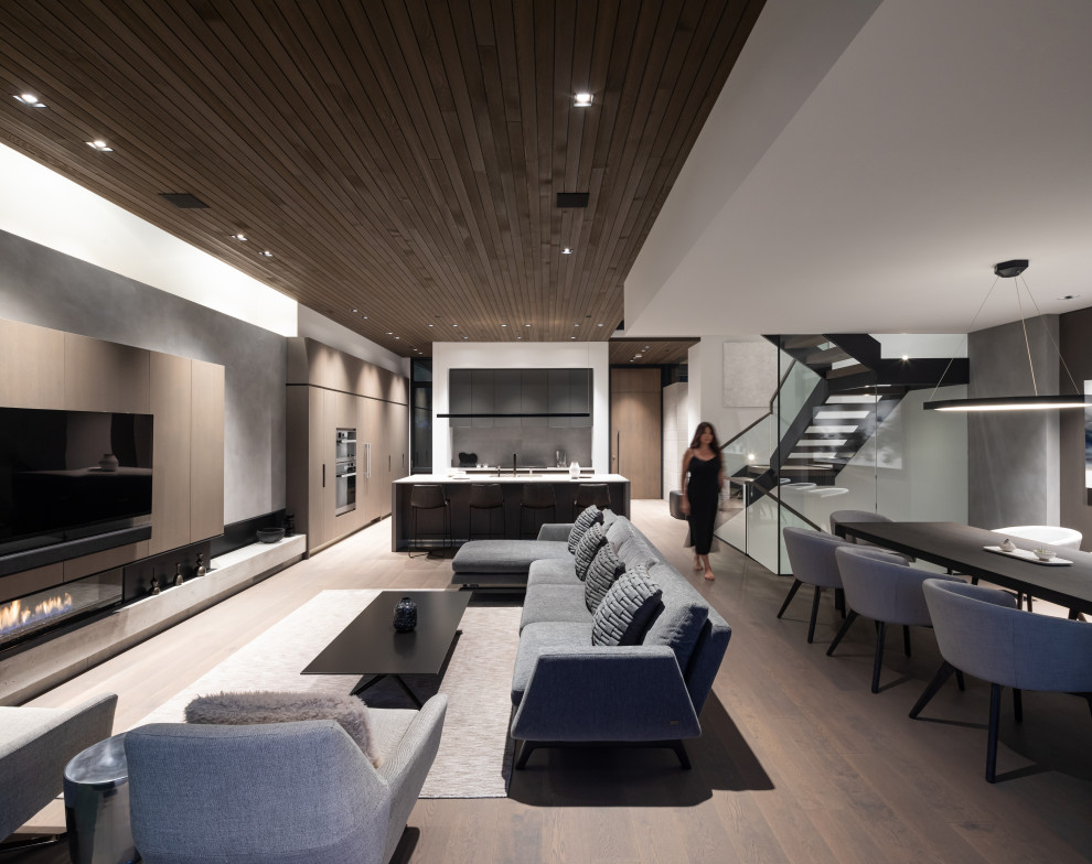 This is an example of a mid-sized contemporary open concept living room in Vancouver with medium hardwood floors, a ribbon fireplace, a plaster fireplace surround, a built-in media wall, grey floor and wood.