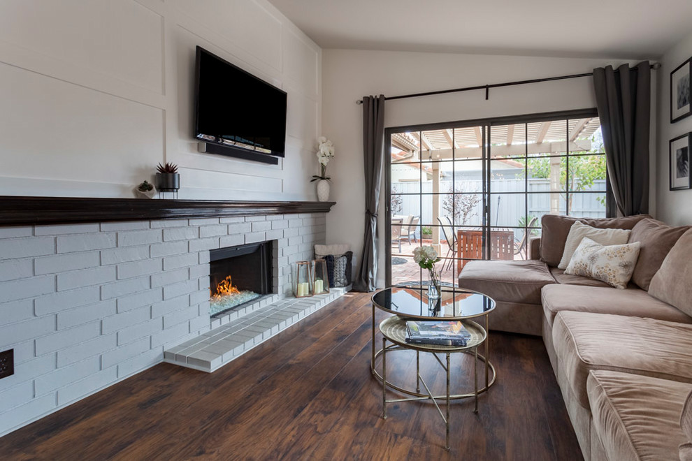 This is an example of a mid-sized transitional open concept family room in Los Angeles with a game room, grey walls, medium hardwood floors, a standard fireplace, a brick fireplace surround, a wall-mounted tv and brown floor.