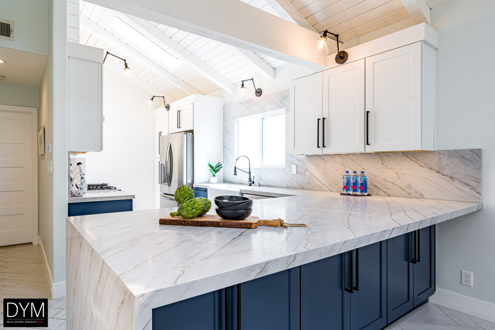 Design ideas for a beach style galley eat-in kitchen in Los Angeles with a farmhouse sink, shaker cabinets, blue cabinets, quartz benchtops, white splashback, engineered quartz splashback, stainless steel appliances, a peninsula, white floor, white benchtop, vaulted and light hardwood floors.