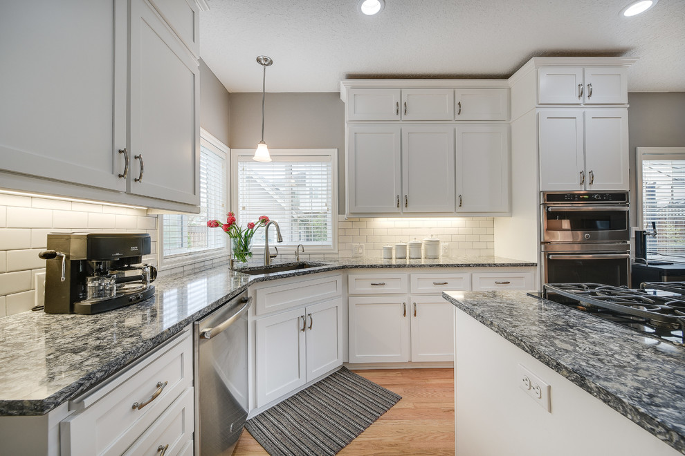 Inspiration for a mid-sized transitional l-shaped light wood floor and brown floor enclosed kitchen remodel in Portland with a drop-in sink, shaker cabinets, white cabinets, quartz countertops, white backsplash, subway tile backsplash, an island and stainless steel appliances