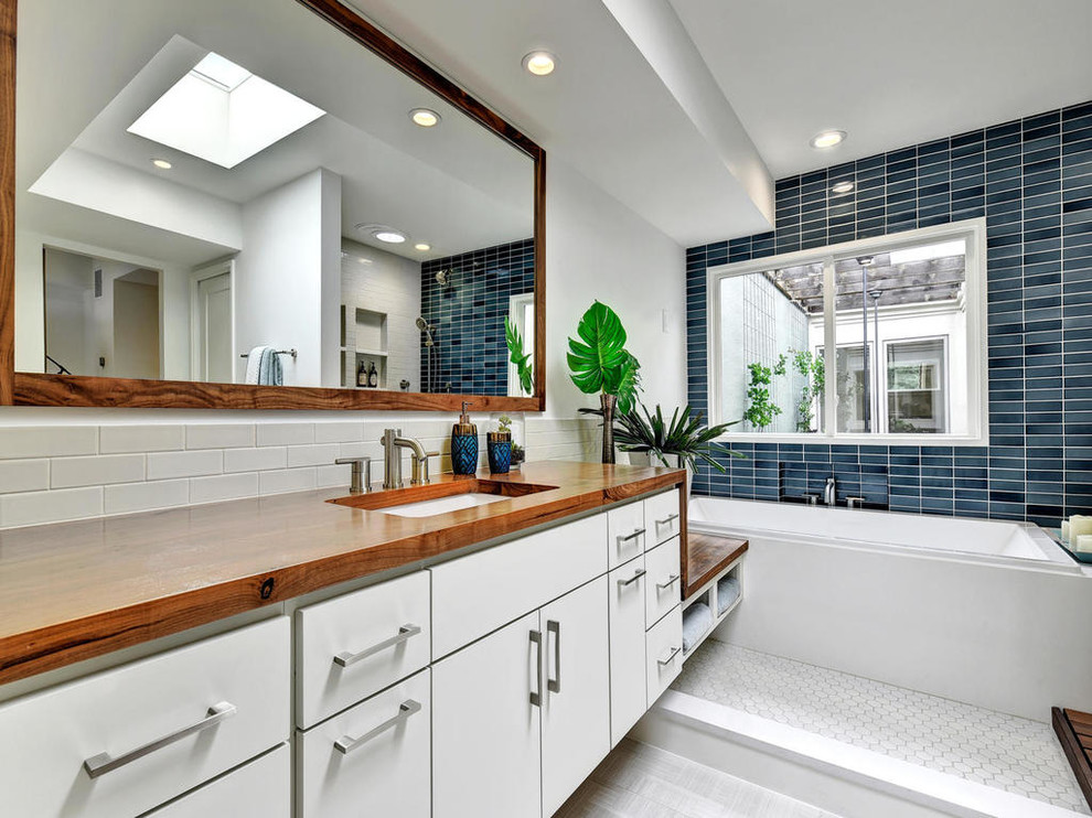 This is an example of a contemporary master bathroom in Austin with flat-panel cabinets, white cabinets, a drop-in tub, blue tile, white walls, an undermount sink, an open shower, ceramic tile, ceramic floors, wood benchtops and an open shower.