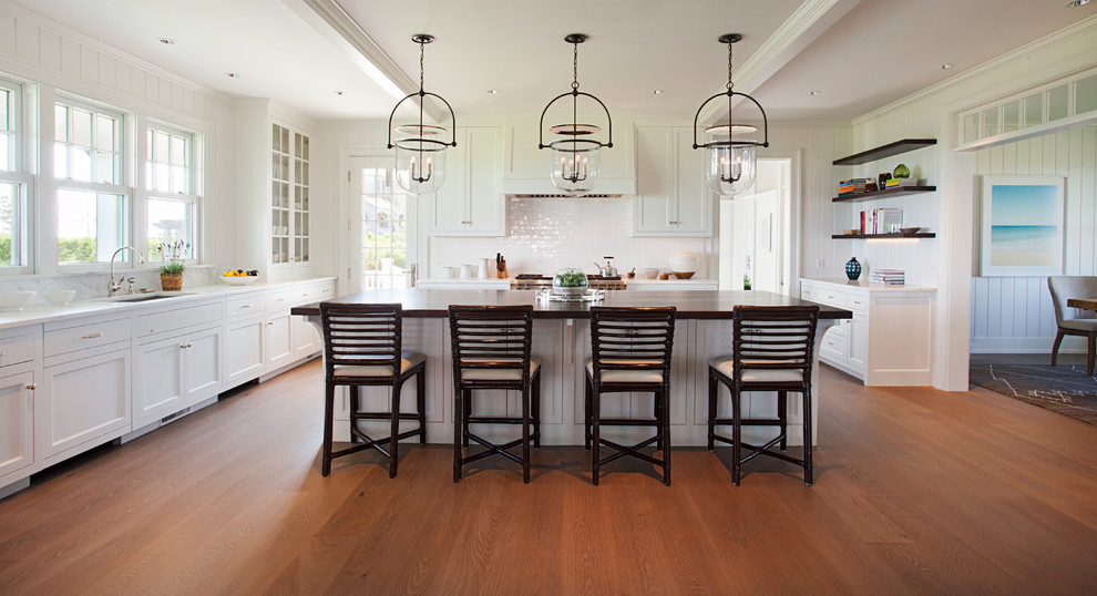 Beach style u-shaped kitchen in Boston with an undermount sink, shaker cabinets, white cabinets, white splashback, medium hardwood floors, with island and brown floor.