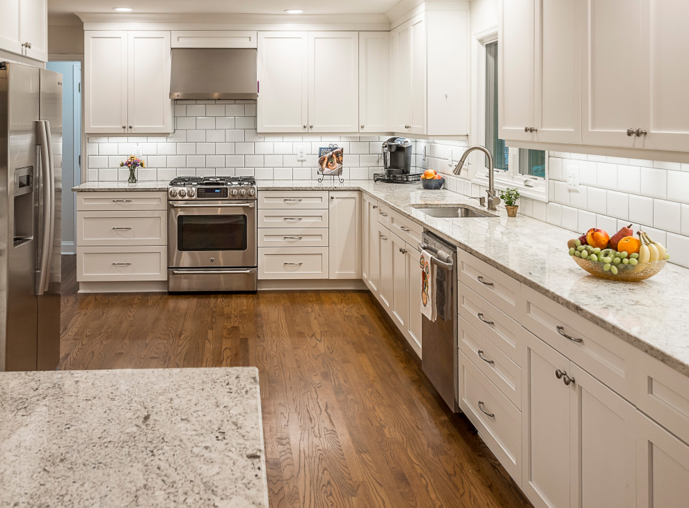 Photo of a mid-sized l-shaped eat-in kitchen in Atlanta with a drop-in sink, recessed-panel cabinets, white cabinets, granite benchtops, white splashback, subway tile splashback, stainless steel appliances, medium hardwood floors, a peninsula, brown floor and yellow benchtop.