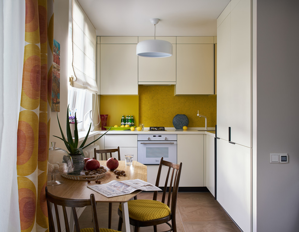 This is an example of a small eclectic l-shaped eat-in kitchen in Yekaterinburg with an undermount sink, flat-panel cabinets, solid surface benchtops, yellow splashback, mosaic tile splashback, white appliances, porcelain floors, brown floor, no island, beige cabinets and beige benchtop.