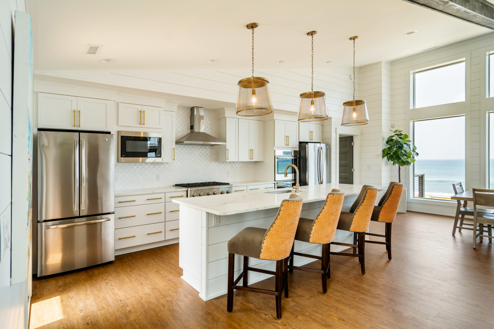 Example of a mid-sized beach style single-wall medium tone wood floor and brown floor open concept kitchen design in Other with an undermount sink, shaker cabinets, white cabinets, white backsplash, stainless steel appliances, an island, white countertops, quartzite countertops and ceramic backsplash