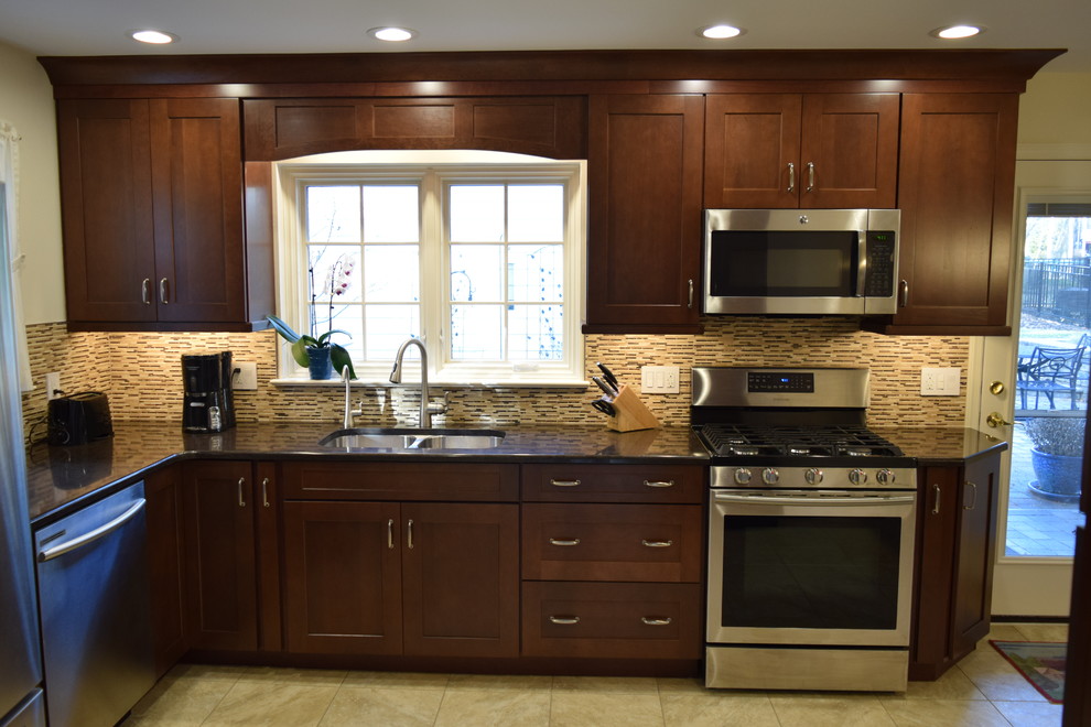 Transitional l-shaped vinyl floor and beige floor kitchen photo with an undermount sink, shaker cabinets, medium tone wood cabinets, quartz countertops, beige backsplash, glass tile backsplash, stainless steel appliances and a peninsula