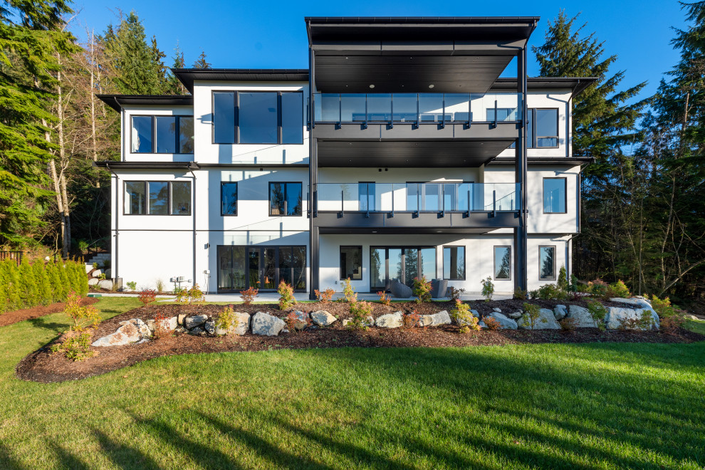 Photo of a large contemporary three-storey stucco white house exterior in Vancouver with a hip roof, a shingle roof and a grey roof.
