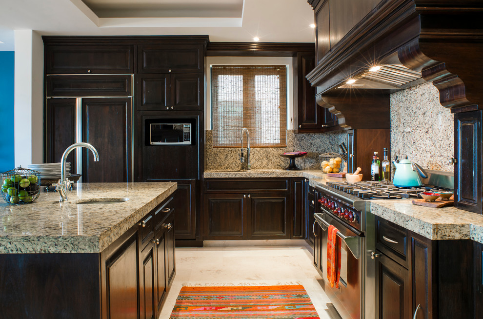 Example of a large island style l-shaped marble floor kitchen pantry design with an undermount sink, raised-panel cabinets, dark wood cabinets, granite countertops, beige backsplash, stainless steel appliances and an island