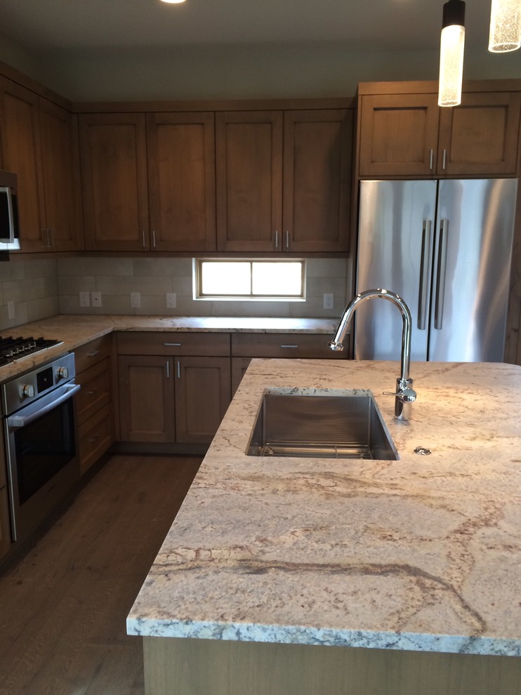 Example of a small transitional l-shaped medium tone wood floor kitchen design with an undermount sink, shaker cabinets, medium tone wood cabinets, granite countertops, beige backsplash, porcelain backsplash, stainless steel appliances and an island