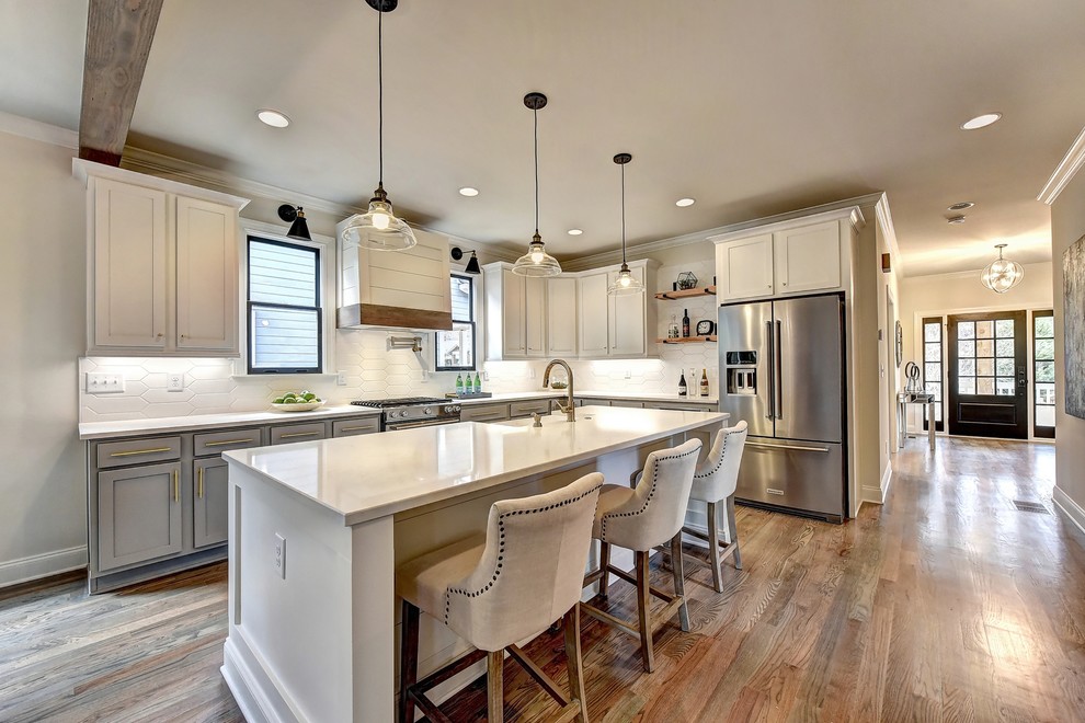 Inspiration for a country l-shaped kitchen in Atlanta with a farmhouse sink, shaker cabinets, white cabinets, white splashback, stainless steel appliances, medium hardwood floors, with island, brown floor and white benchtop.
