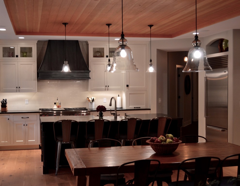 Large transitional u-shaped light wood floor and beige floor eat-in kitchen photo in Boston with a farmhouse sink, shaker cabinets, white cabinets, soapstone countertops, white backsplash, ceramic backsplash, stainless steel appliances and an island