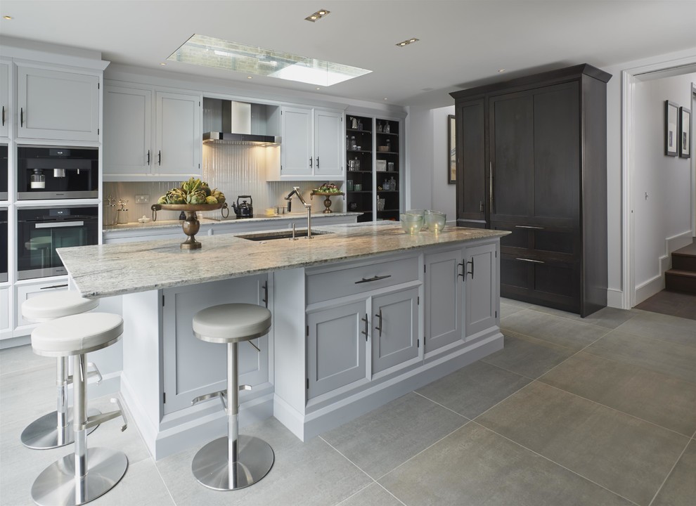 Mid-sized transitional kitchen in London with with island, an undermount sink, grey cabinets, granite benchtops, grey floor, shaker cabinets and black appliances.