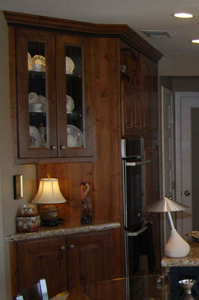 Mid-sized transitional u-shaped medium tone wood floor open concept kitchen photo with an undermount sink, raised-panel cabinets, medium tone wood cabinets, granite countertops, beige backsplash, stone tile backsplash, stainless steel appliances, beige walls and an island