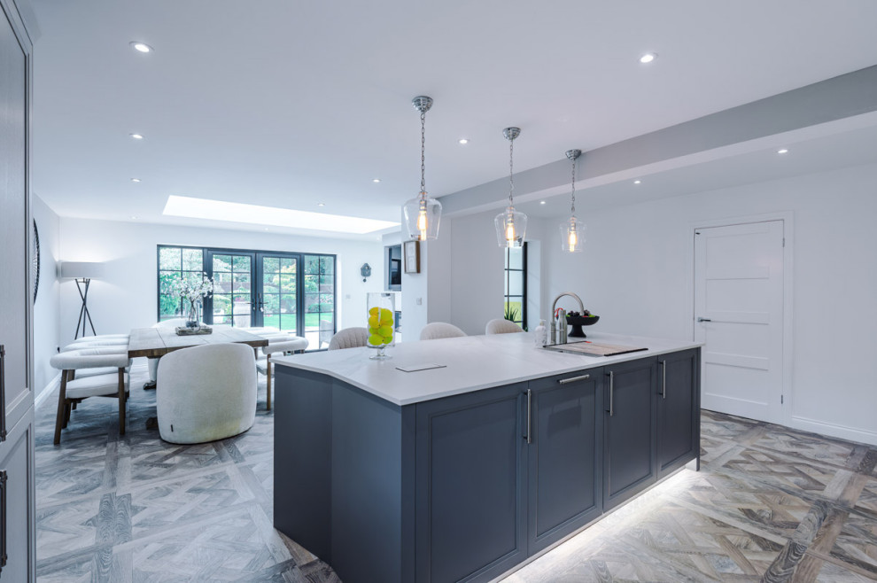This is an example of a large contemporary open plan kitchen in Manchester with a built-in sink, shaker cabinets, engineered quartz splashback, stainless steel appliances and white worktops.