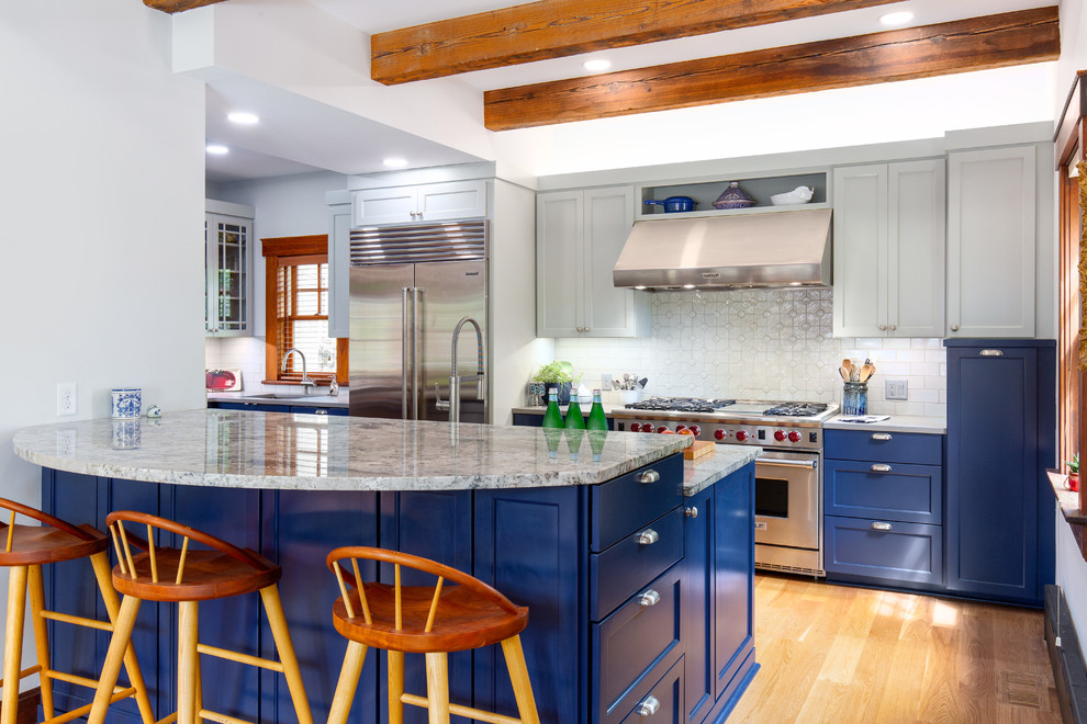 Mid-sized arts and crafts galley kitchen in Kansas City with a farmhouse sink, shaker cabinets, blue cabinets, granite benchtops, white splashback, mosaic tile splashback, stainless steel appliances, medium hardwood floors, grey benchtop, a peninsula and brown floor.