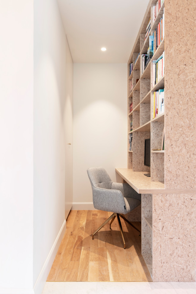 Exempel på ett litet industriellt hemmabibliotek, med vita väggar, ljust trägolv, ett inbyggt skrivbord och brunt golv