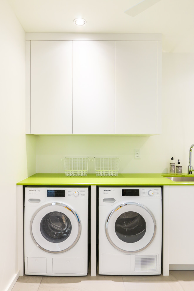 Photo of a small modern single-wall dedicated laundry room in Atlanta with an undermount sink, flat-panel cabinets, white cabinets, solid surface benchtops, white walls, slate floors, a side-by-side washer and dryer, beige floor and green benchtop.