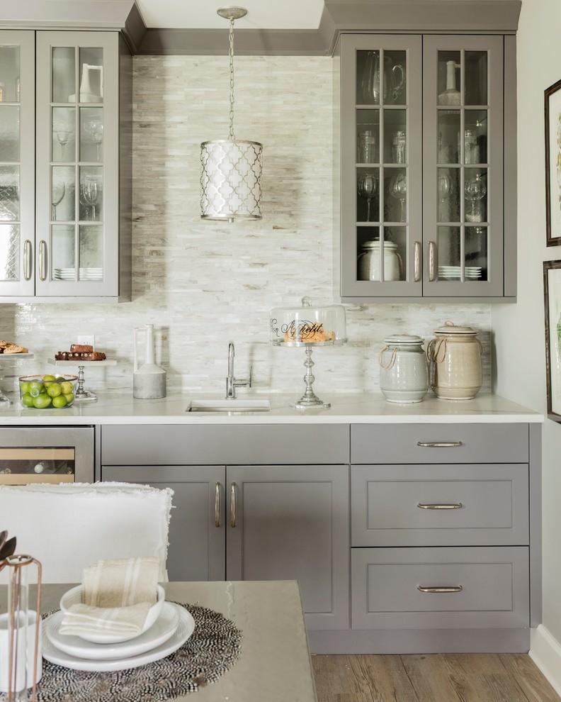 Design ideas for a transitional single-wall wet bar in DC Metro with an undermount sink, glass-front cabinets, grey cabinets, beige splashback, matchstick tile splashback, light hardwood floors and beige floor.