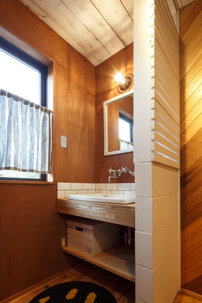 Photo of a midcentury powder room in Other with open cabinets, white tile, brown walls, medium hardwood floors, a drop-in sink, wood benchtops and brown floor.