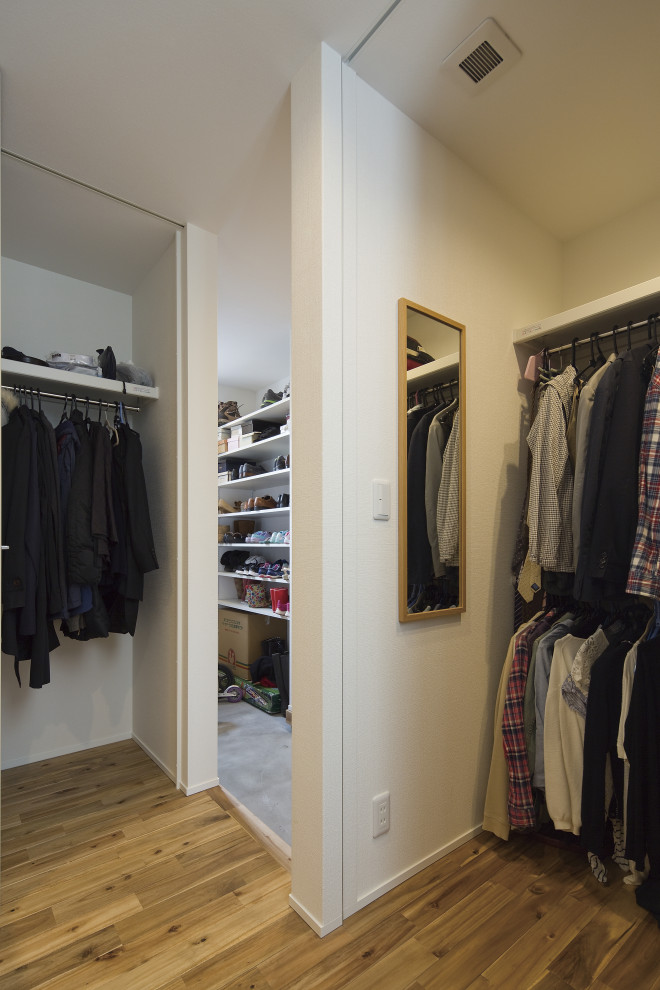 Photo of a mid-sized modern gender-neutral walk-in wardrobe in Tokyo Suburbs with open cabinets, white cabinets, light hardwood floors, brown floor and wallpaper.
