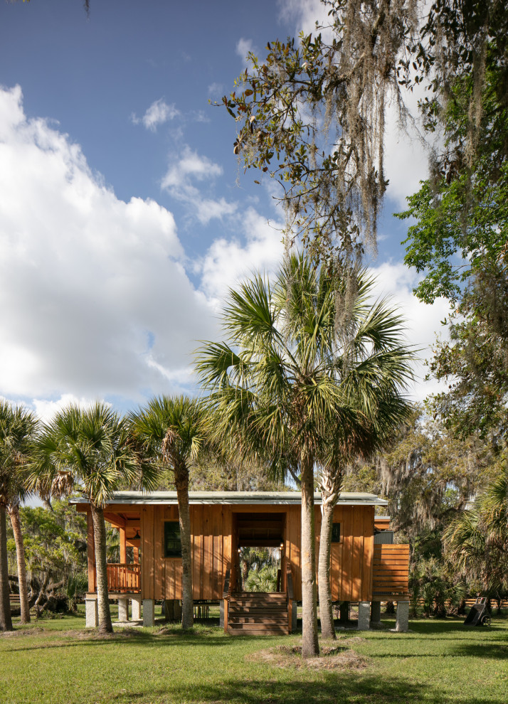 Small cottage brown one-story wood and board and batten exterior home photo in Tampa with a metal roof and a gray roof