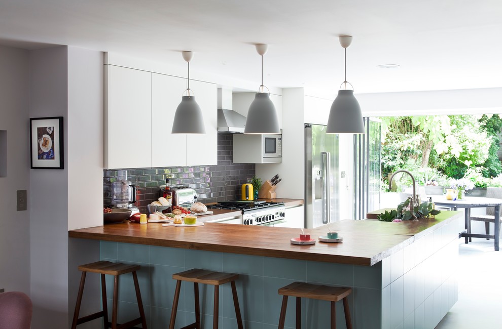 Inspiration for a contemporary kitchen in London with flat-panel cabinets, white cabinets, black splashback, subway tile splashback and stainless steel appliances.