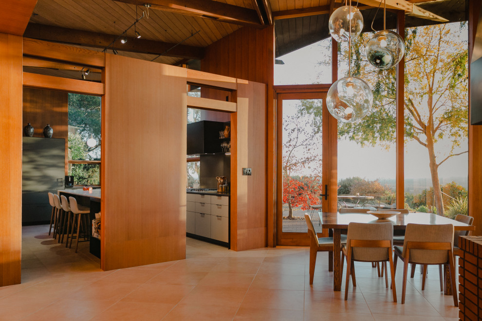 This is an example of a midcentury open plan dining in San Francisco with exposed beam, vaulted, wood and beige floor.