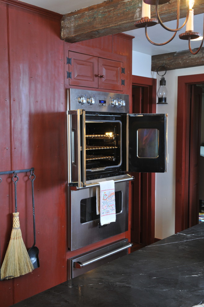 Mid-sized mountain style l-shaped medium tone wood floor and beige floor kitchen photo in Orange County with a farmhouse sink, raised-panel cabinets, red cabinets, soapstone countertops, beige backsplash, subway tile backsplash, stainless steel appliances and an island