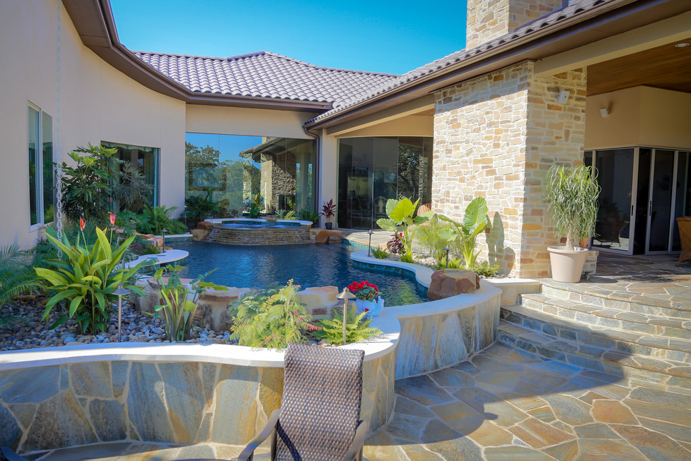 Design ideas for a mid-sized mediterranean courtyard custom-shaped pool in Austin with a hot tub and natural stone pavers.