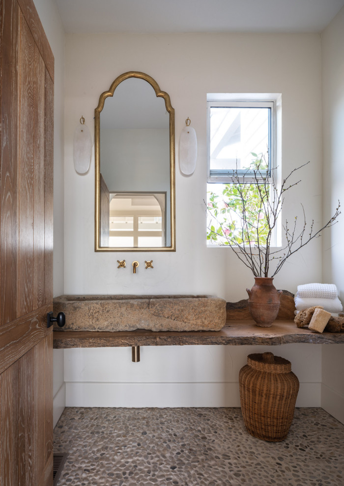 Photo of a powder room in Los Angeles with white walls, pebble tile floors, a vessel sink, wood benchtops, grey floor and brown benchtops.