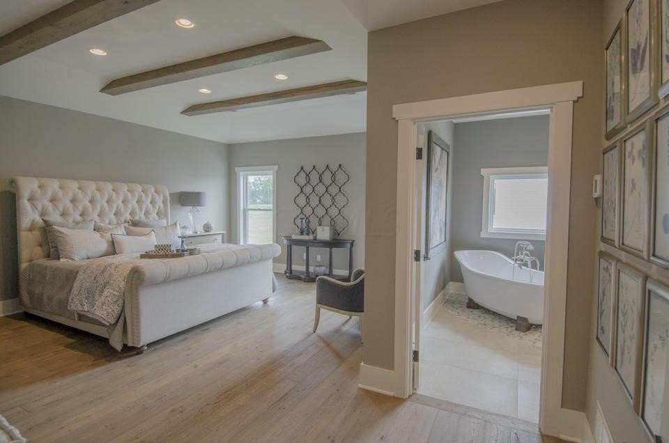 This is an example of a transitional master bedroom in Columbus with beige walls, light hardwood floors and exposed beam.