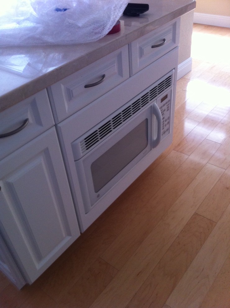 Inspiration for a transitional light wood floor kitchen remodel with recessed-panel cabinets, white cabinets, quartz countertops, stone tile backsplash, white appliances and an island