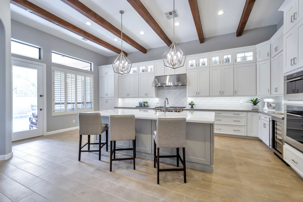 Inspiration for a large transitional l-shaped porcelain tile and brown floor eat-in kitchen remodel in Phoenix with a farmhouse sink, shaker cabinets, white cabinets, quartz countertops, white backsplash, subway tile backsplash, stainless steel appliances, an island and gray countertops