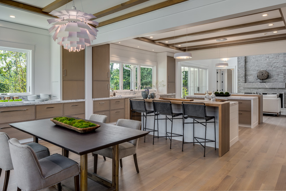This is an example of a transitional open plan kitchen in New York with marble benchtops, marble splashback, medium hardwood floors, multiple islands, brown floor, recessed-panel cabinets, medium wood cabinets, white splashback and white benchtop.