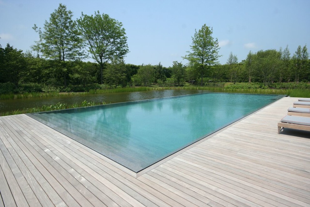 This is an example of a contemporary backyard rectangular infinity pool in New York with decking.