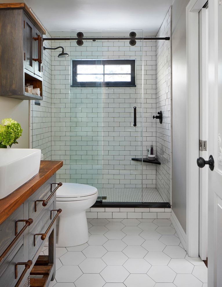 Mid-sized country 3/4 bathroom in Denver with flat-panel cabinets, blue cabinets, an alcove shower, a two-piece toilet, grey walls, ceramic floors, a vessel sink, wood benchtops, white floor, a sliding shower screen, brown benchtops, white tile and subway tile.