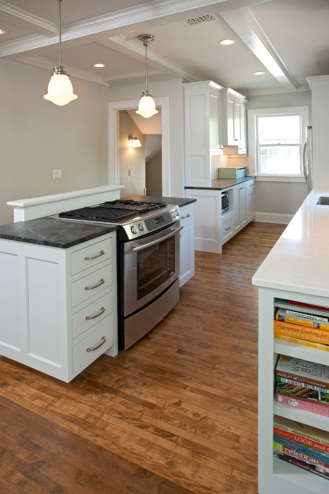 Small arts and crafts galley eat-in kitchen in Minneapolis with a single-bowl sink, recessed-panel cabinets, soapstone benchtops, green splashback, glass tile splashback, stainless steel appliances, medium hardwood floors, with island, beige floor and white cabinets.