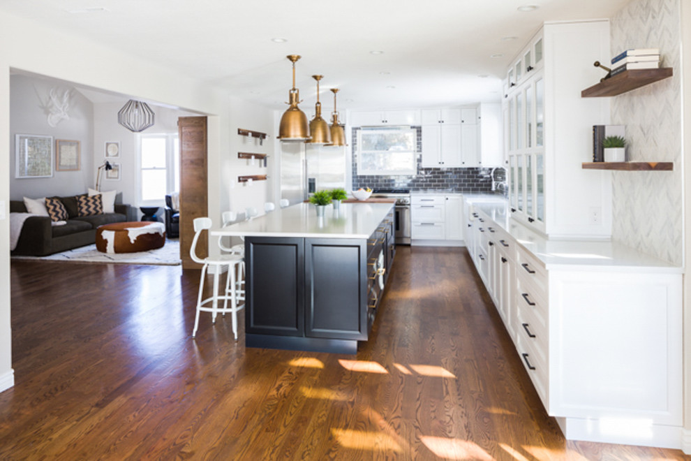 This is an example of a large country l-shaped eat-in kitchen in Denver with a farmhouse sink, recessed-panel cabinets, black cabinets, wood benchtops, grey splashback, subway tile splashback, stainless steel appliances, medium hardwood floors and with island.