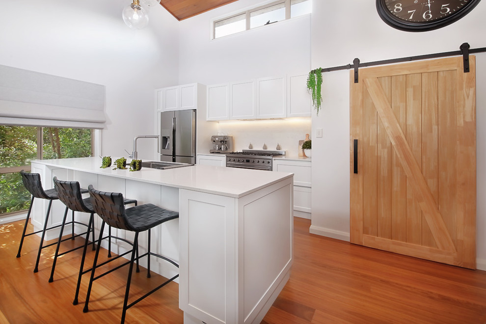Inspiration for a large modern single-wall open plan kitchen in Sydney with a drop-in sink, recessed-panel cabinets, yellow cabinets, quartz benchtops, white splashback, glass sheet splashback, stainless steel appliances, light hardwood floors, with island, brown floor and white benchtop.