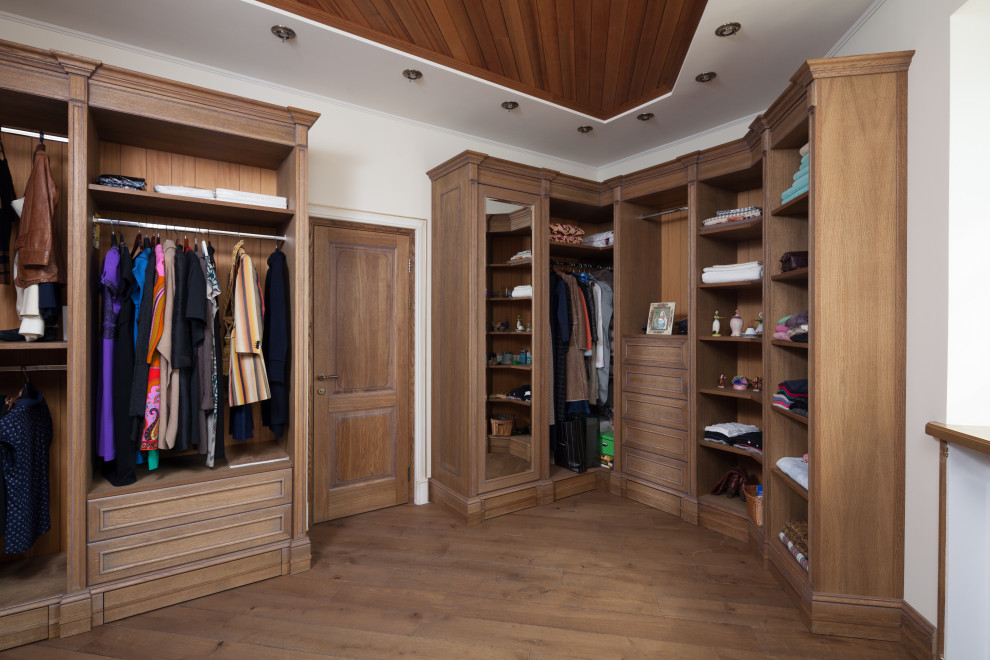 Photo of a large traditional gender-neutral walk-in wardrobe in Moscow with recessed-panel cabinets, distressed cabinets and dark hardwood floors.