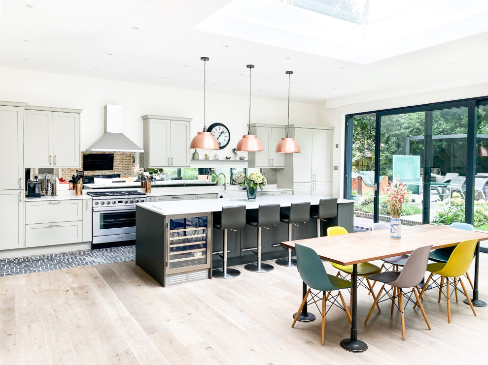 Photo of a large contemporary l-shaped open plan kitchen in London with an undermount sink, shaker cabinets, grey cabinets, marble benchtops, metallic splashback, glass sheet splashback, stainless steel appliances, medium hardwood floors, with island, brown floor and white benchtop.
