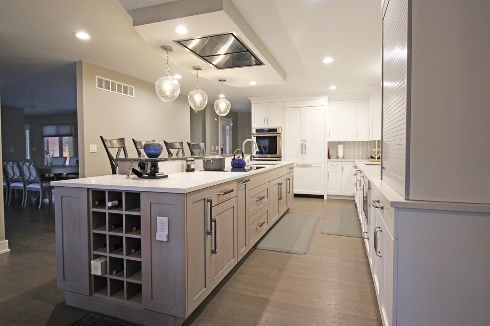 Photo of a large transitional l-shaped eat-in kitchen in Detroit with an undermount sink, shaker cabinets, white cabinets, quartz benchtops, grey splashback, marble splashback, stainless steel appliances, dark hardwood floors, with island, brown floor and white benchtop.