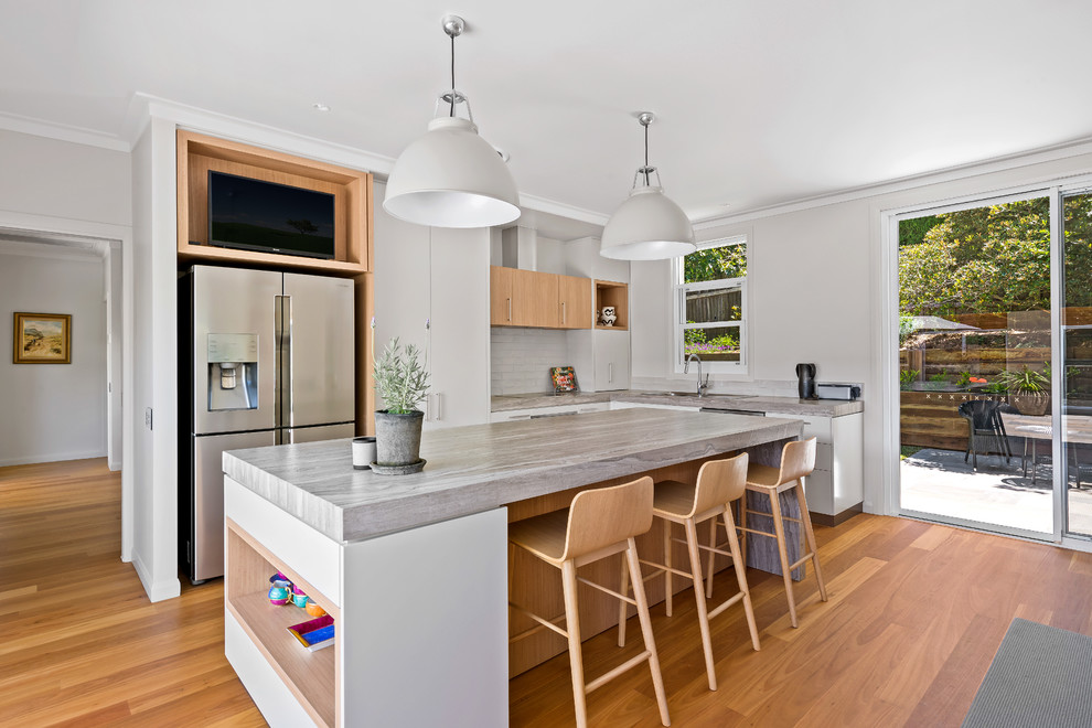 Inspiration for a contemporary l-shaped eat-in kitchen in Other with a drop-in sink, flat-panel cabinets, white cabinets, white splashback, stainless steel appliances, medium hardwood floors, with island, brown floor and grey benchtop.