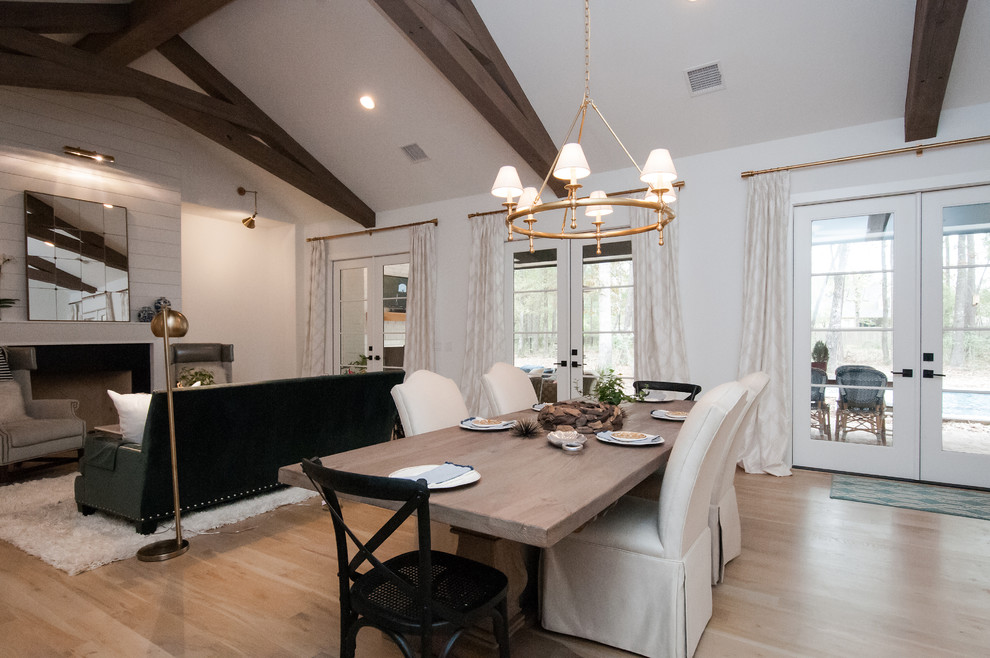 This is an example of a large transitional open plan dining in Houston with white walls, light hardwood floors, a standard fireplace, beige floor and a wood fireplace surround.
