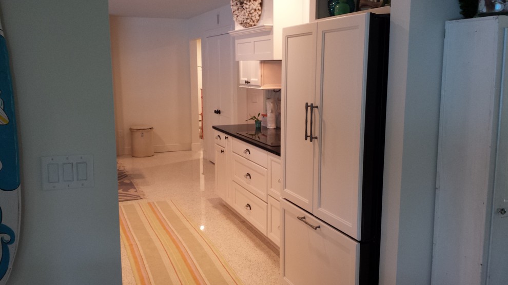 Example of a transitional galley kitchen design in Tampa with a farmhouse sink, recessed-panel cabinets, white cabinets, granite countertops, beige backsplash, glass tile backsplash, paneled appliances and black countertops
