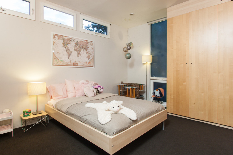 This is an example of a modern kids' bedroom for kids 4-10 years old and girls in Los Angeles with beige walls, carpet and black floor.