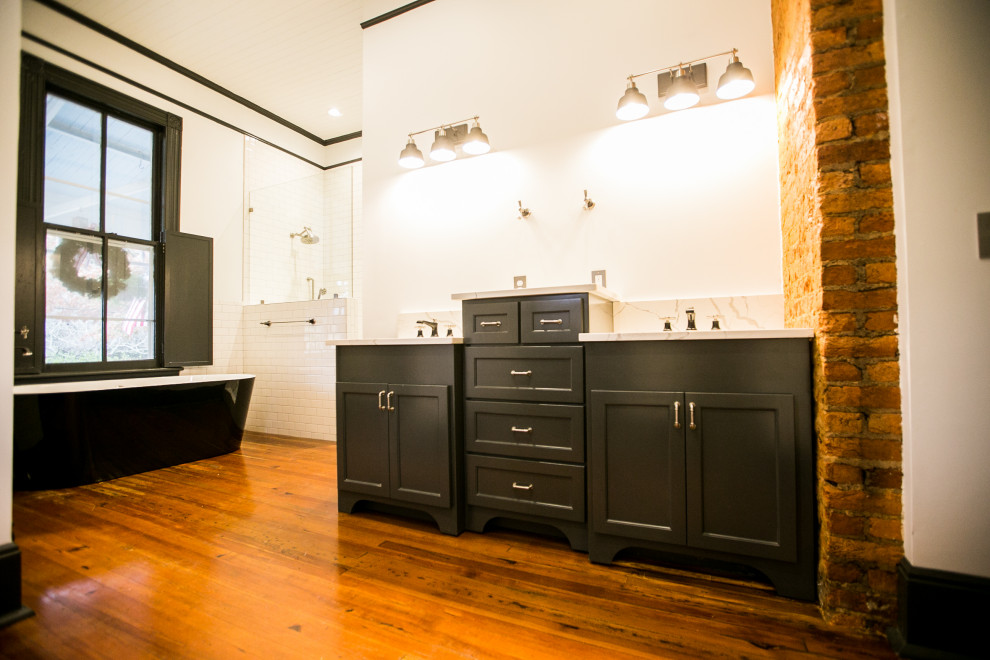 This is an example of a large traditional master bathroom in Other with recessed-panel cabinets, black cabinets, a freestanding tub, white tile, subway tile, white walls, medium hardwood floors, a drop-in sink, brown floor, white benchtops, a double vanity and a built-in vanity.
