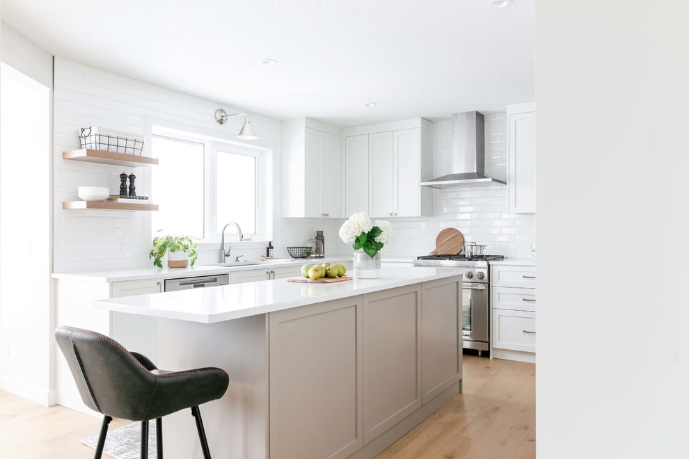 Large transitional u-shaped medium tone wood floor and brown floor eat-in kitchen photo in Calgary with an undermount sink, shaker cabinets, white cabinets, quartzite countertops, white backsplash, subway tile backsplash, stainless steel appliances, an island and white countertops
